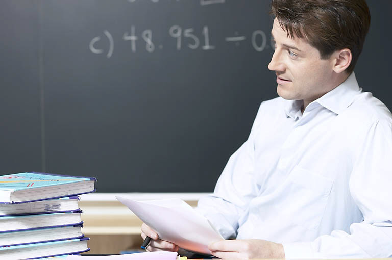 teacher sitting by desk in front of blackboard